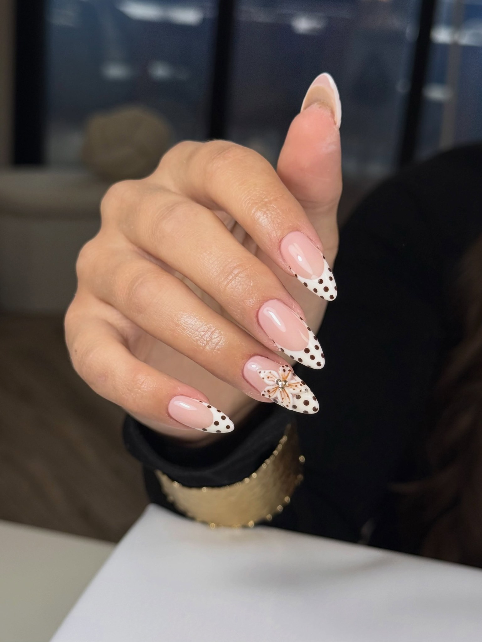 Nude amandelnagels met zwarte stipjes op de tips en een bedeltje