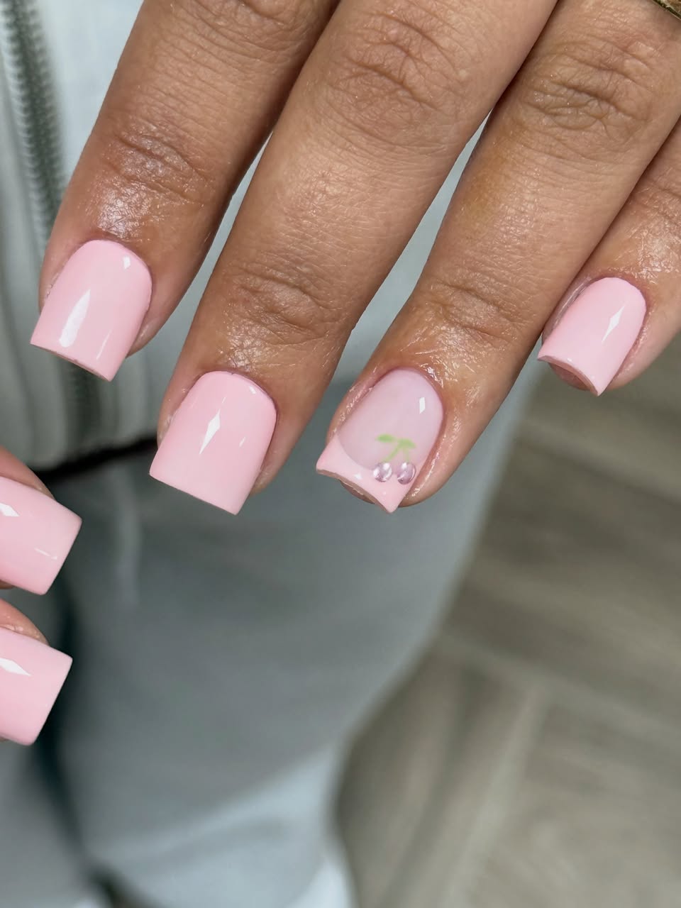 Close-up van pastelroze nagels met een kersje als nailart